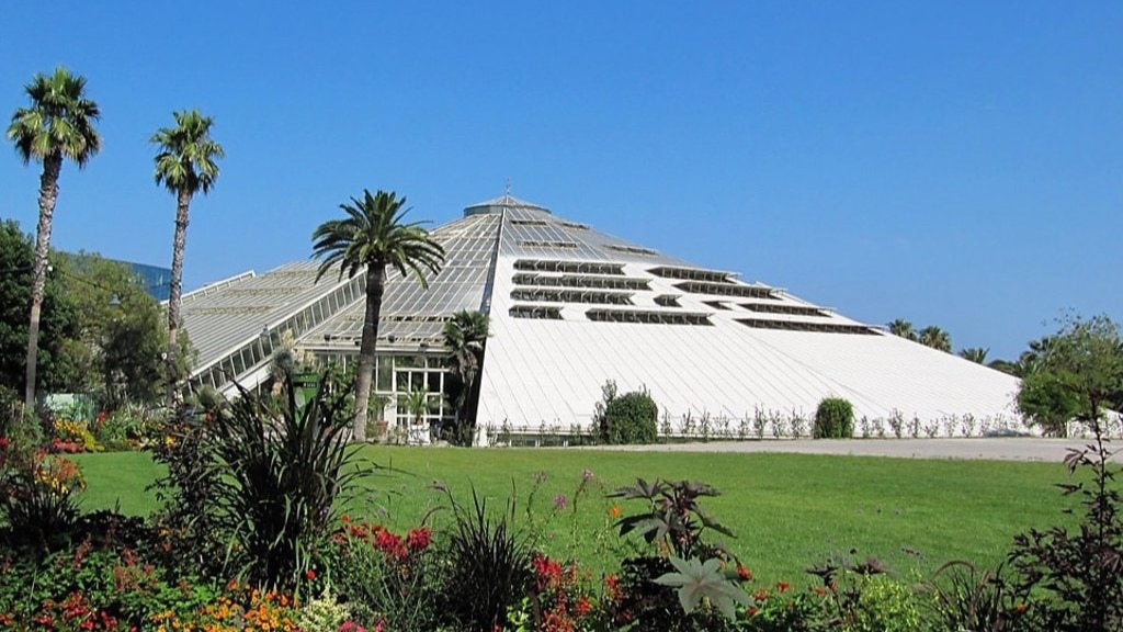 La grande serre pyramidale du Parc Phoenix entourée de palmiers et de jardins fleuris.